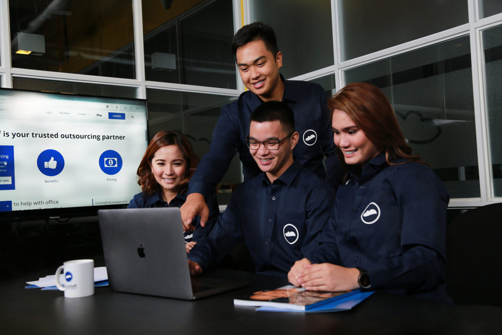 Cloudstaff professionals working together in front of a laptop with books, documents, and a mug on the table.