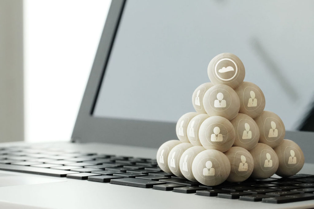 Wooden balls stacked like a pyramid on a laptop's keyboard. Each ball has a 2D man print. The one on top has Cloudstaff logo.