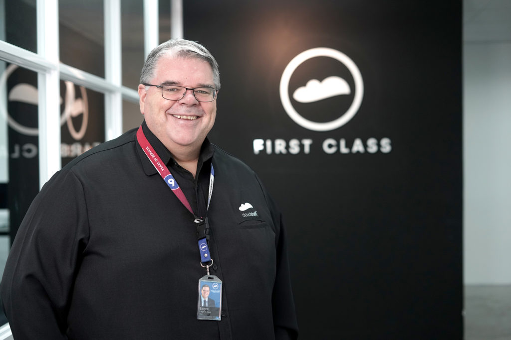 A portrait of Cloudstaff CEO Lloyd Ernst in front of the First Class Lounge signage with the company logo.