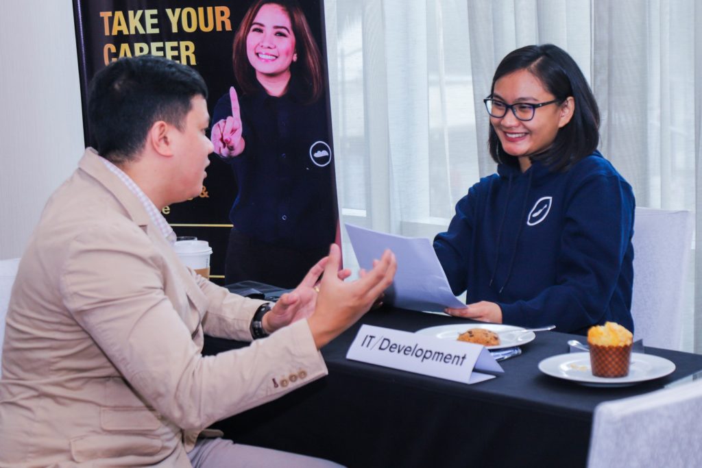 A man and woman talking over a desk. The woman, a Cloudstaff employee, is holding a document while the man is talking.