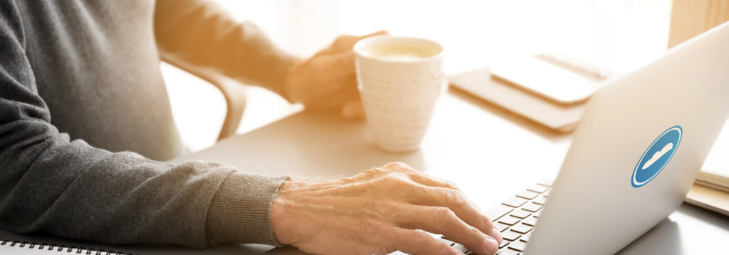 Photo of a man's hands on an office desk. Their right one is placed on a keyboard and the left is holding a mug.