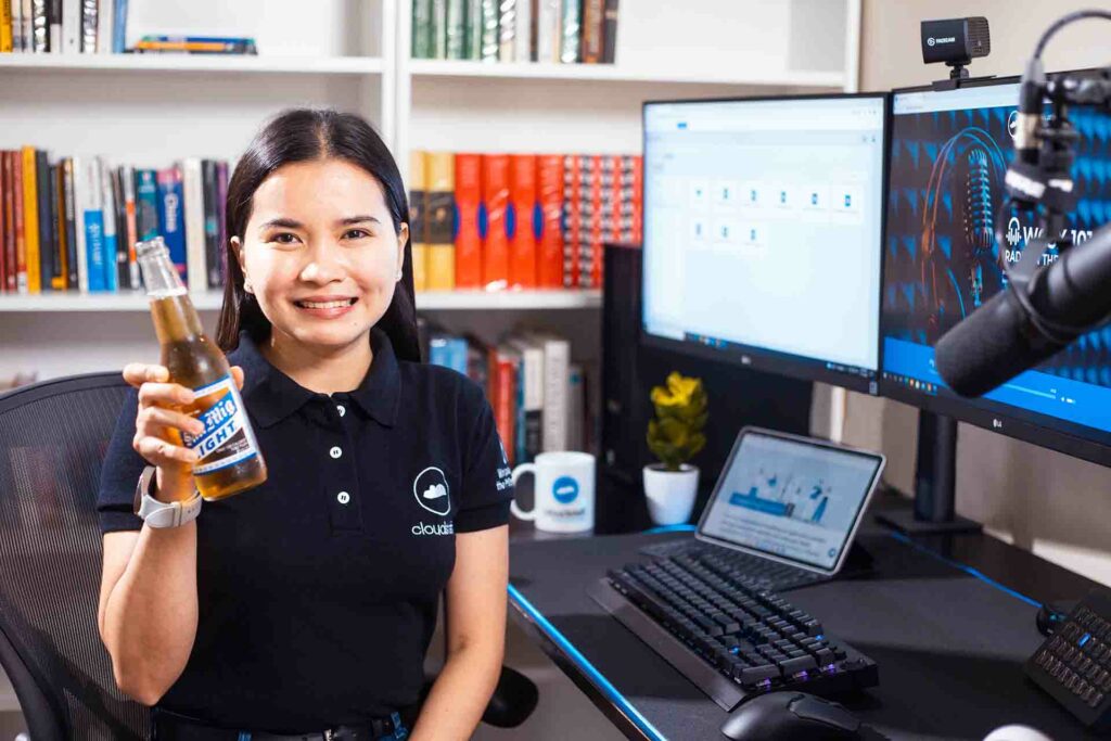 A female Cloudstaffer with a beer beside a computer desk setup