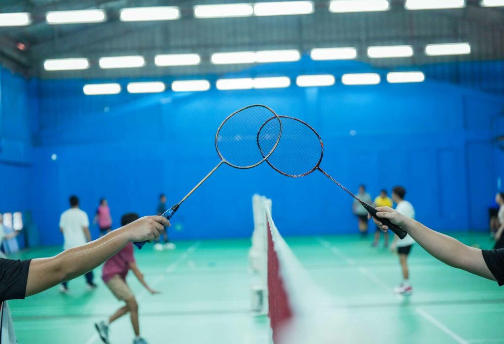 Two badminton players making their rackets touch over the net