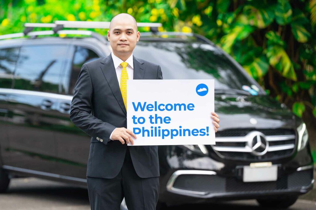 Another man in suit holding a signage that reads "Welcome to the Philippines" beside a car.